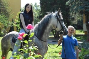 O tânără călare pe un cal ținut de ham de un bărbat.