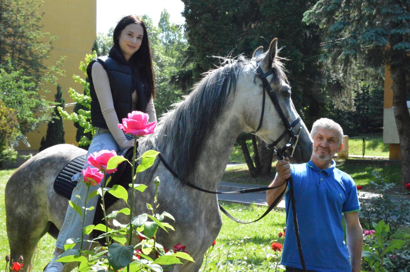 O tânără călare pe un cal ținut de ham de un bărbat.