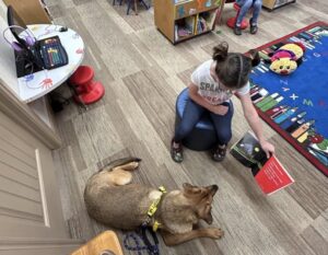 Un copil cu o carte în mână, alături de un câine