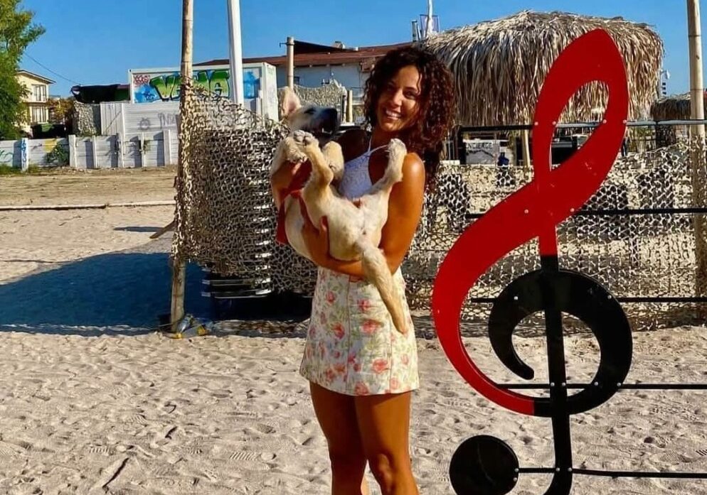 Ionela Guzic ține în brațe un câine, pe plajă.