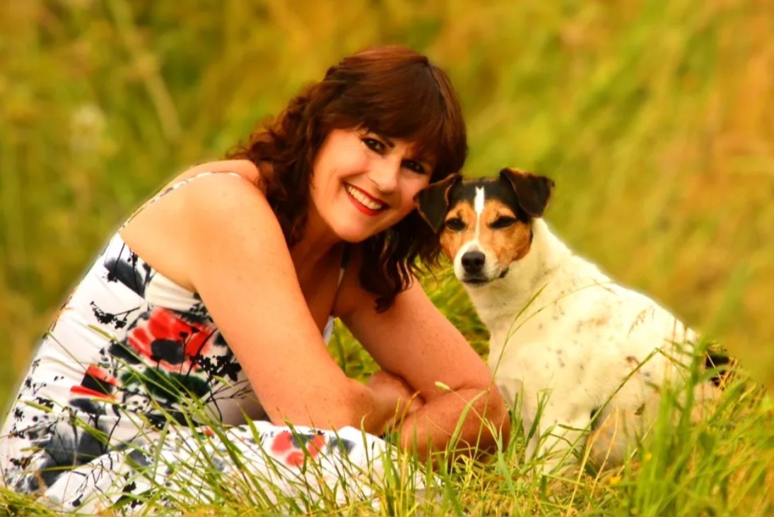 O femeie și un câine pozează în iarbă