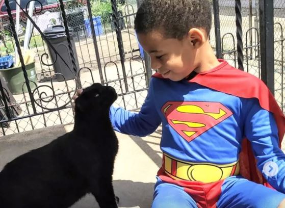 Un copil îmbrăcat în costumul lui Superman, alături de o pisică neagră