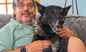 Un bărbat stă pe canapea și își ține câinele în brațe