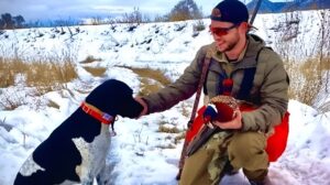 Un câine în zăpadă alături de un bărbat îmbrăcat în camuflaj