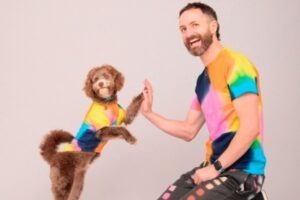 Bărbat care zâmbește, fiind asortat cu cățelul său în haine colorate și bătând palma