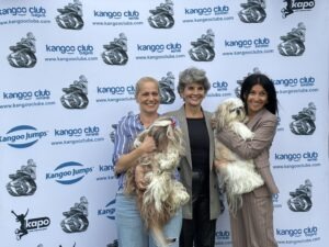 Trei femei alături de căței în fața unui panou publicitar