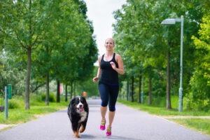 Un câine și stăpâna lui aleargă pe aleea unui parc