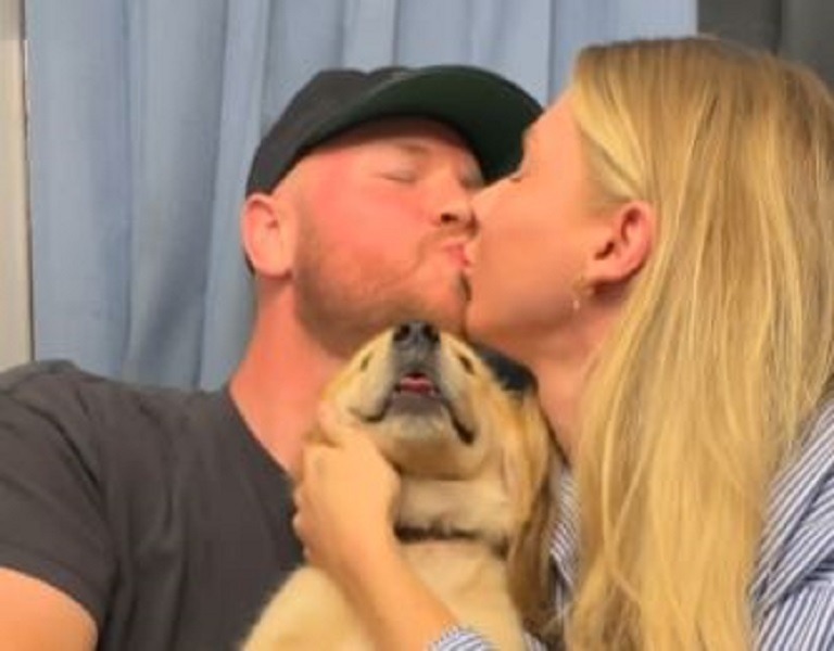 Un cuplu se sărută în timp ce își ține cățelul în brațe