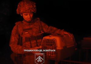 Un soldat ucrainean ține în mână o cușcă în care se află o pisică