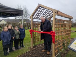 Un bărbat taie o panglică roșie în timp ce copiii aplaudă