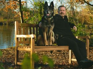 Actorul RIcky Gervais stă pe o bancă, alături de câinele lui