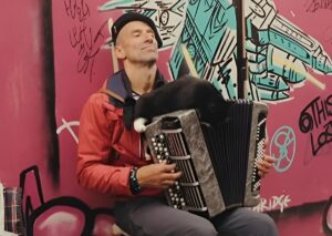 Un muzician cântă la acordeon pe o stradă din Paris, în timp ce pe instrumentul muzical stă o pisică