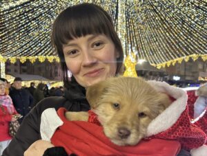 O femeie ține un câine în brațe, la un târg de Crăciun