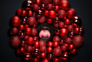 Un câine cu limba scoasă stă în spatele unui aranjament de Crăciun