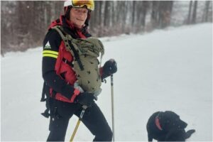 Un salvamontist cu bebelușul în port-bebe, alături de un câine negru